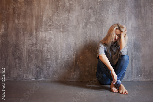 Sad woman sits on the floor. Depression and chronic fatigue. Young beautiful blonde in a gray sweater and jeans