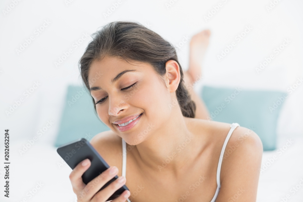 Smiling woman looking at mobile phone in bed Smiling woman looking at mobile phone in bed