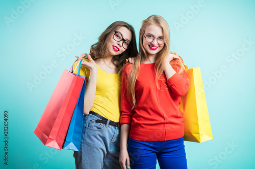 Two happy young women with shopping bags on blue background look with smile.