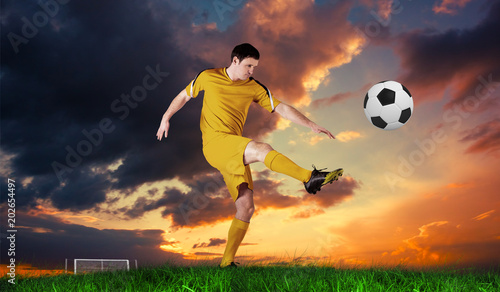Football player in yellow kicking against green grass under blue sky