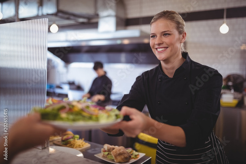 Attractive young female chef giving fresh Greek salad to waiter photo