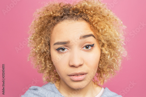Close up of pretty face of the girl. She is doubting and she is in frustration. Girl is keeping her one brow up on the forehead. Isolated on pink background.