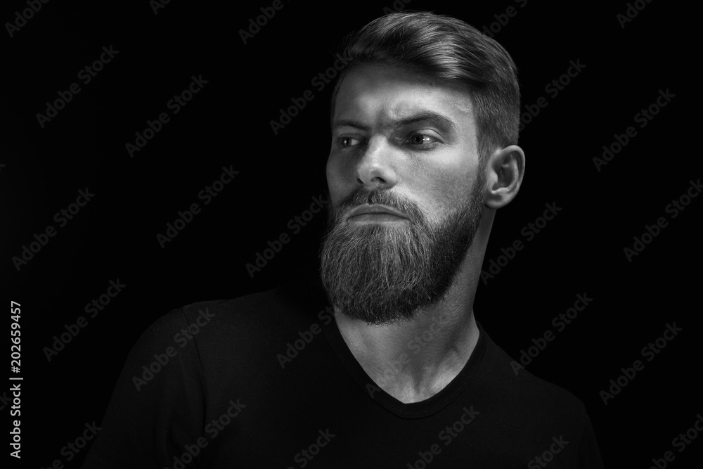 Portrait of handsome single bearded young man with serious expression looking over black background with copy space