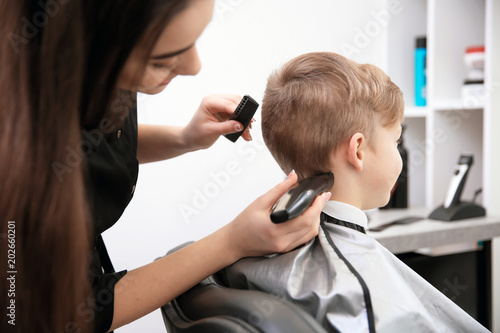 Professional female hairdresser working with little boy in salon