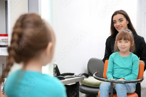 Professional female hairdresser working with little girl in salon