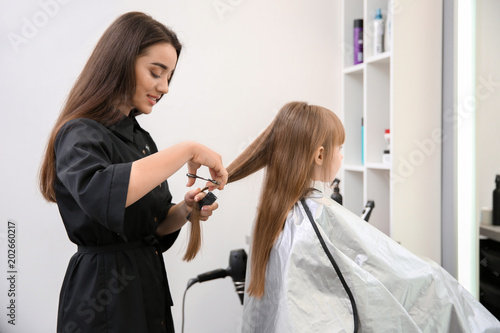 Professional female hairdresser working with little girl in salon