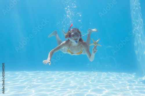 Cute blonde underwater in the swimming pool with snorkel and starfish