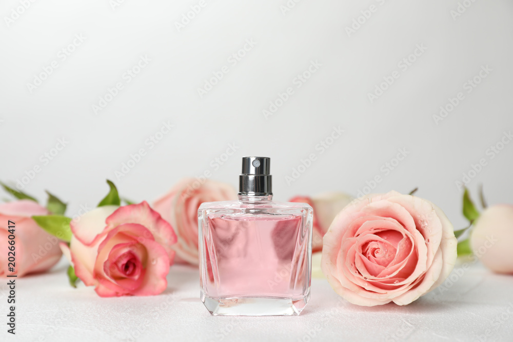 Perfume bottle and flowers on table against light background Perfume bottle and flowers on table against light background