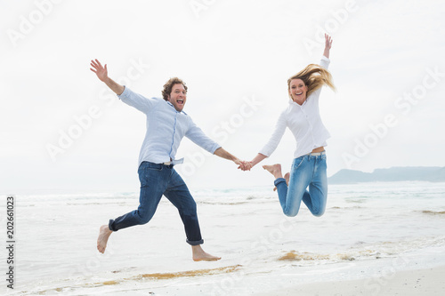 Cheerful couple holding hands and jumping at beach