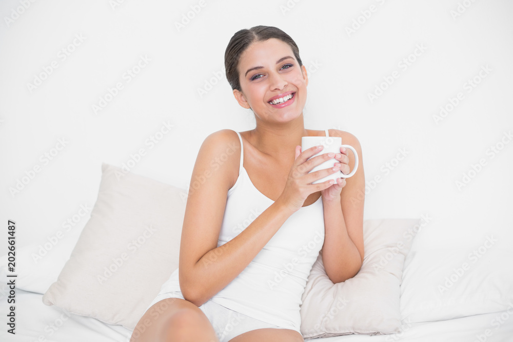 Attractive young brown haired model in white pajamas drinking coffee Attractive young brown haired model in white pajamas drinking coffee