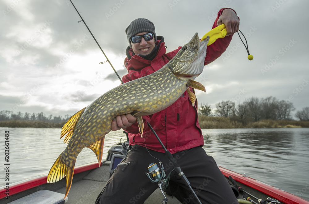 Happy fisherman with big pike fish trophy at the boat with fishing tackles - obrazy, fototapety, plakaty 