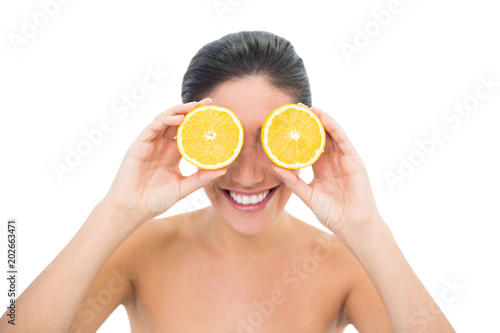 Pretty brunette holding two orange halves over her eyes