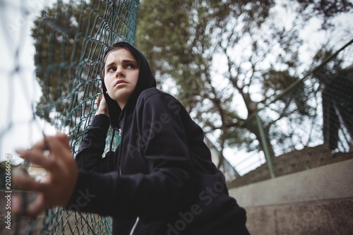 Anxious teenage girl leaning on wire mesh fence