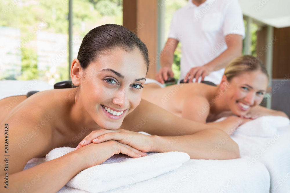 Pretty friends lying on massage tables with hot stones on their backs Pretty friends lying on massage tables with hot stones on their backs