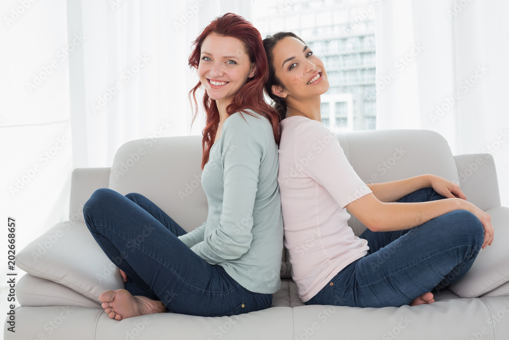 Smiling female friends sitting back-to-back at home Smiling female friends sitting back-to-back at home