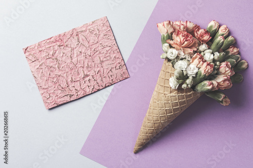 Composition of waffle cone with spring cloves bouquet on purple and blue the background with greetings red card . Flat lay, top view. Place for inscription. Mothers day, anniversary, greetings.