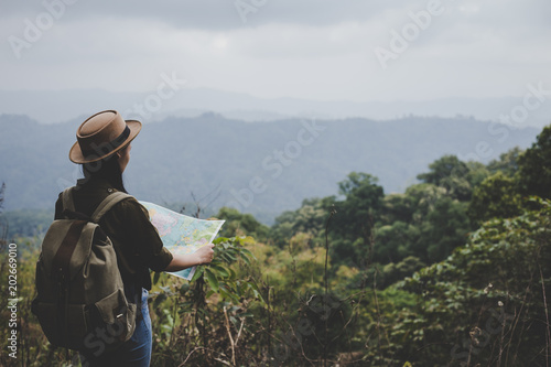Asian woman traveler with backpack checks map to find directions in forest, Travel Concep.