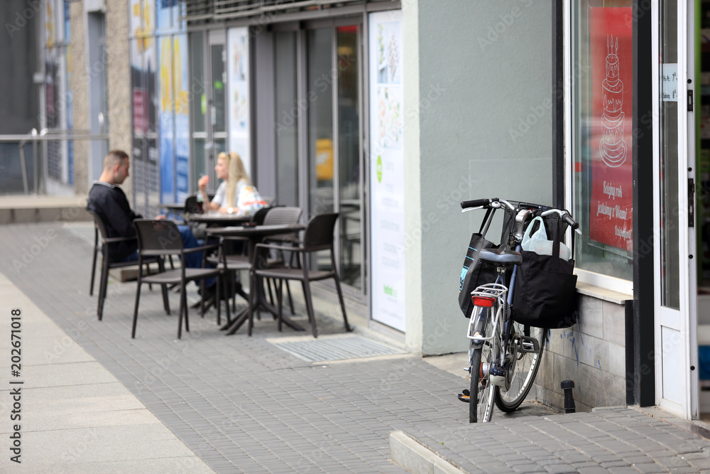 Rower z torbami przed sklepem, kobieta i mężczyzna przy stoliku przed restauracją.