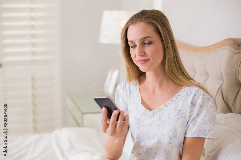 Natural calm woman sitting in bed holding smartphone Natural calm woman sitting in bed holding smartphone