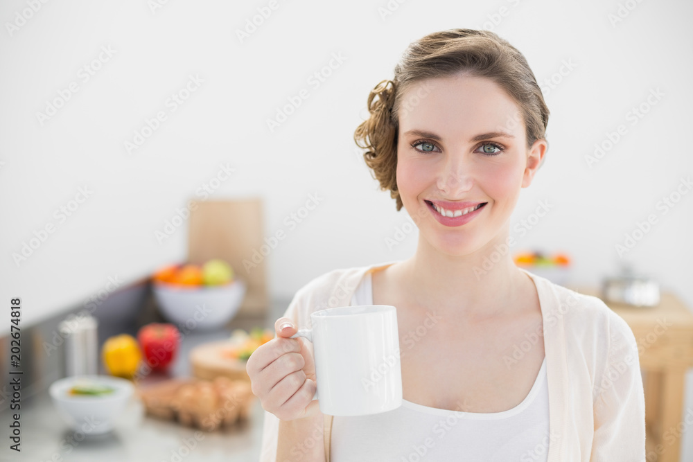 Cheerful lovely woman standing in her kitchen holding a cup Cheerful lovely woman standing in her kitchen holding a cup