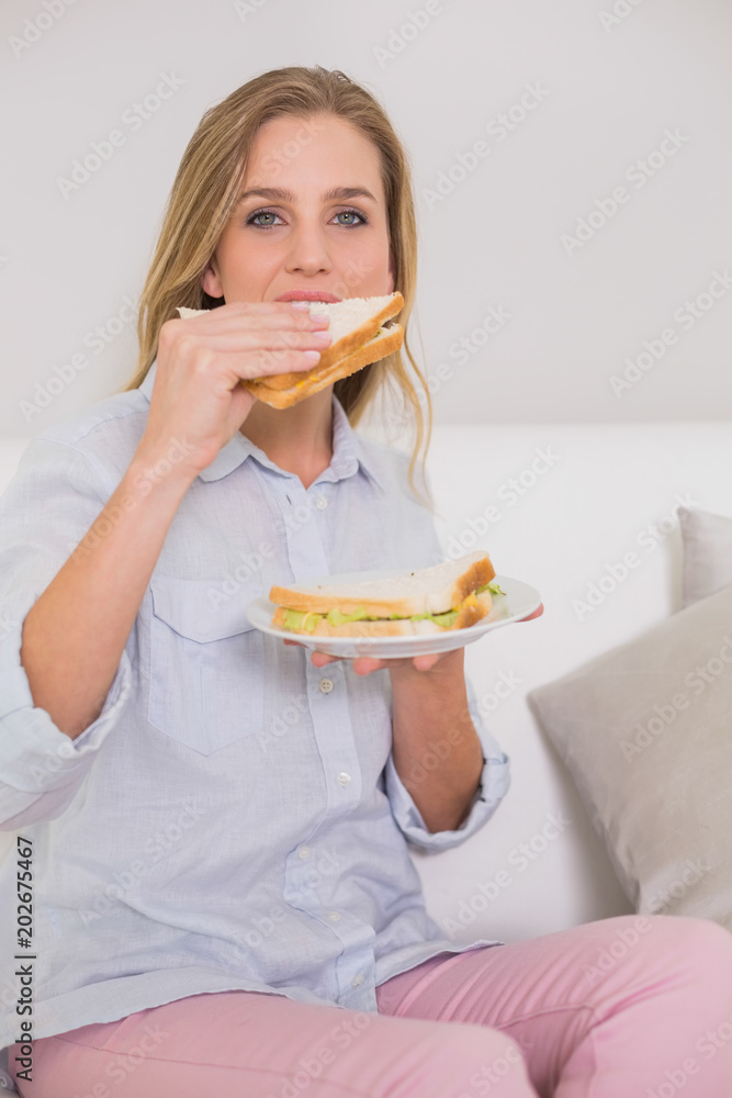 Happy casual blonde sitting on couch eating sandwich Happy casual blonde sitting on couch eating sandwich