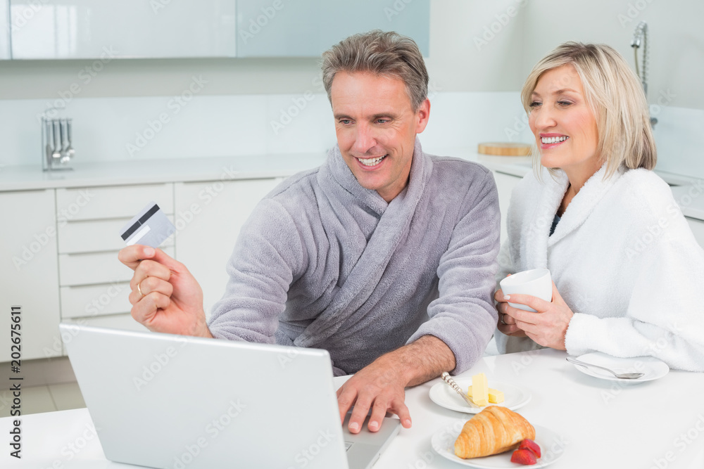 Couple in bathrobes doing online shopping in kitchen Couple in bathrobes doing online shopping in kitchen