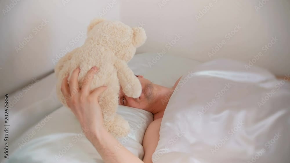 Young father dad wakes up and finds a toy bear in bed after a hard night with a child. Young father dad wakes up and finds a toy bear in bed after a hard night with a child.