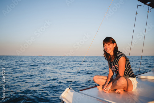 Young pretty smiling woman in striped shirt and white shorts at luxury yacht in sea, sunset © Iryna Budanova