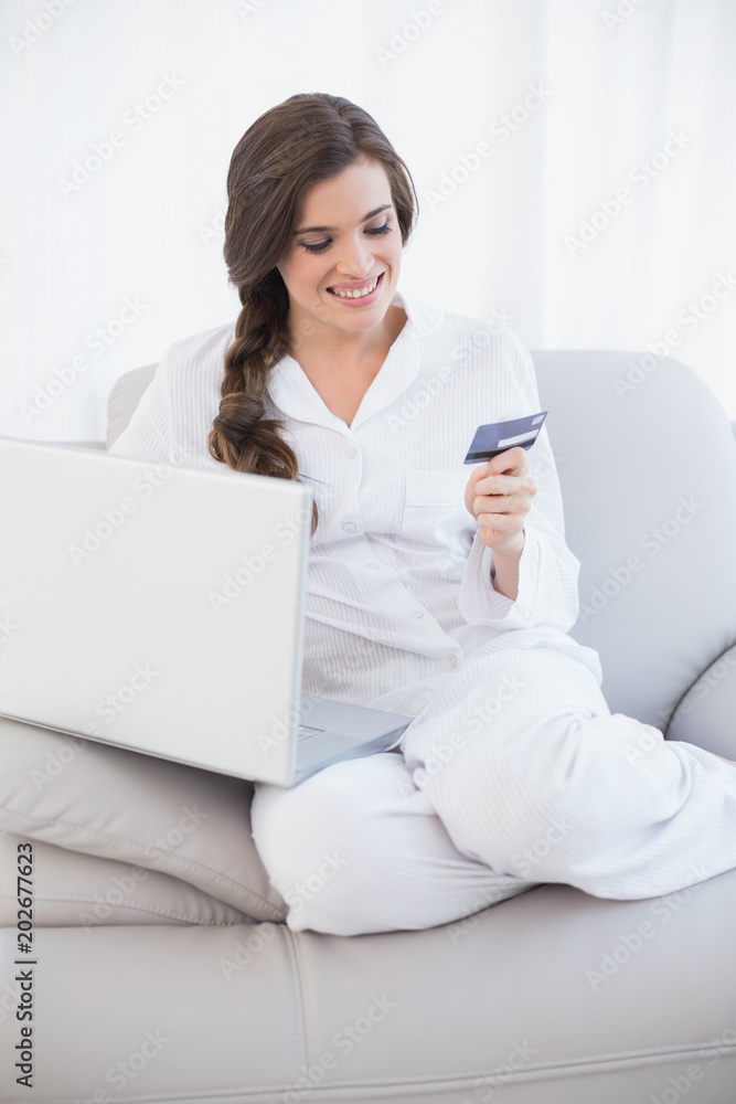 Attractive casual brown haired woman in white pajamas shopping online with her laptop Attractive casual brown haired woman in white pajamas shopping online with her laptop