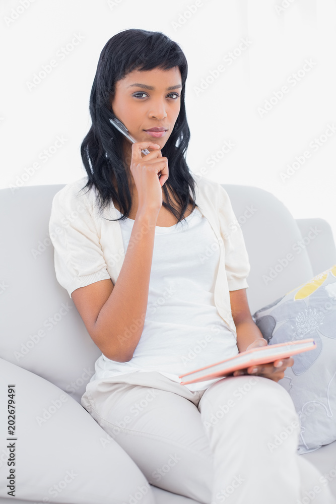 Pensive black haired woman in white clothes writing on a notebook Pensive black haired woman in white clothes writing on a notebook