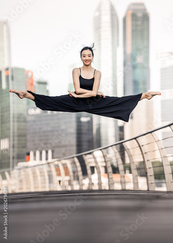 фотографія Cute Young woman athlete with beautiful smile performs a perfect straddle leap h