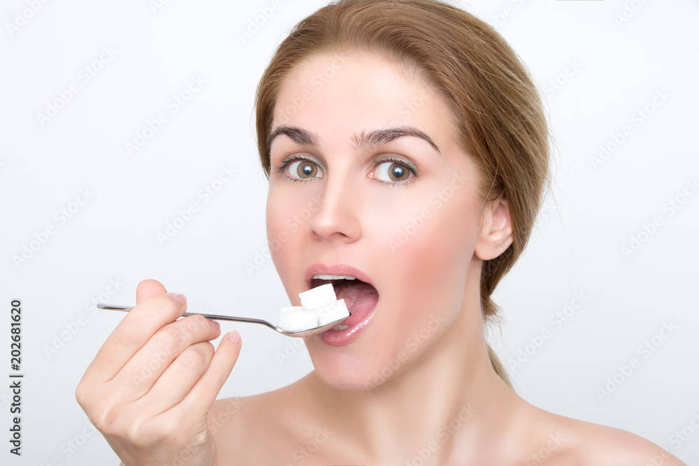 Beautiful woman face leads spoon with sugar cubes into her open mouth Beautiful woman face leads spoon with sugar cubes into her open mouth