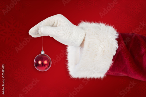 Santas hand is holding a Christmas bulb against red background