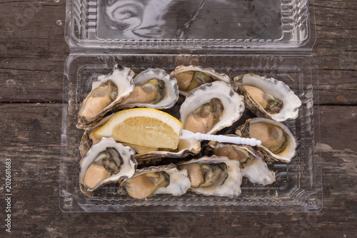 Directly above view of a dozen freshly shelled oysters with lemon in plastic container on wooden table (selective focus)