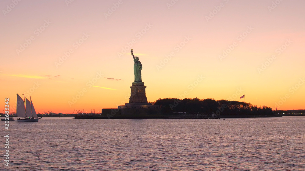Lady Liberty monument in New York Harbor against gorgeous fiery orange sunset