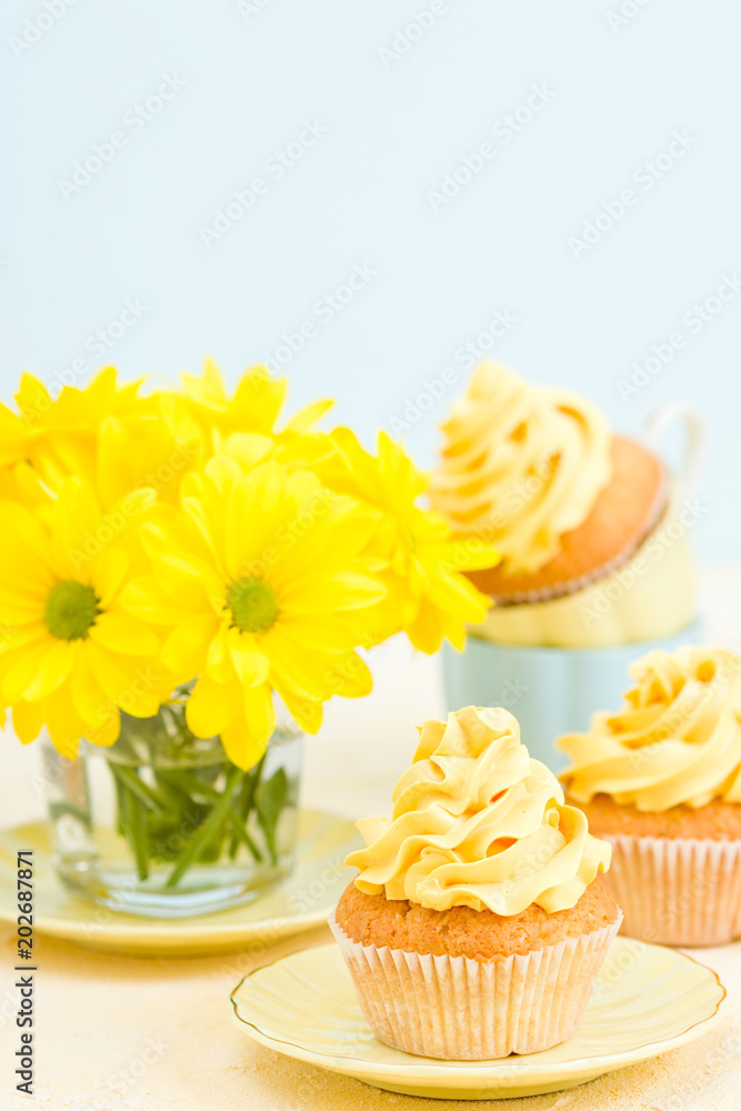 Cupcake with yellow cream decoration and bouquet of yellow chrysanthemum in glass on tender pastel background. Cupcake with yellow cream decoration and bouquet of yellow chrysanthemum in glass on tender pastel background.