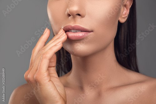 Close up of female person with naked shoulders touching her lips. Isolated on background