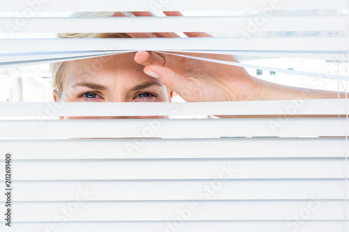 Curious blonde woman looking through venetian blind photo