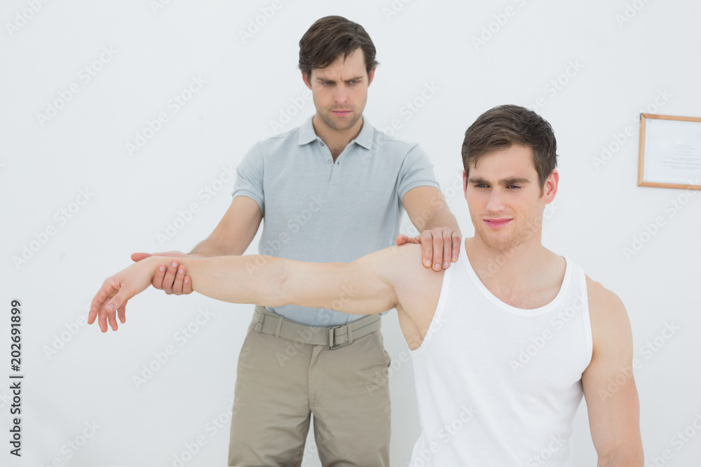 Male physiotherapist examining a young mans arm Male physiotherapist examining a young mans arm
