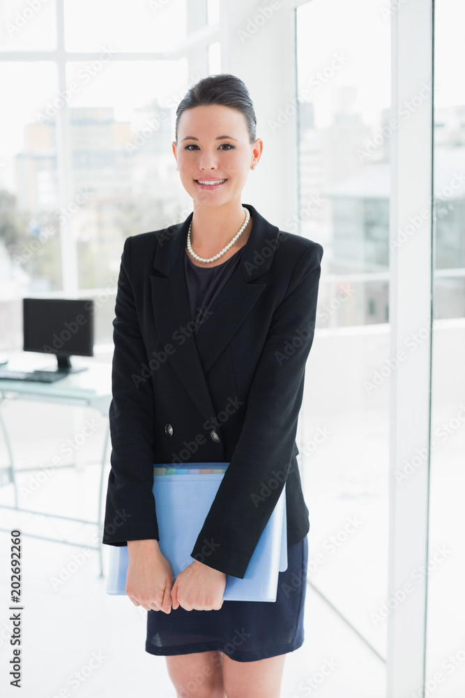 Elegant businesswoman standing with folder in office Elegant businesswoman standing with folder in office