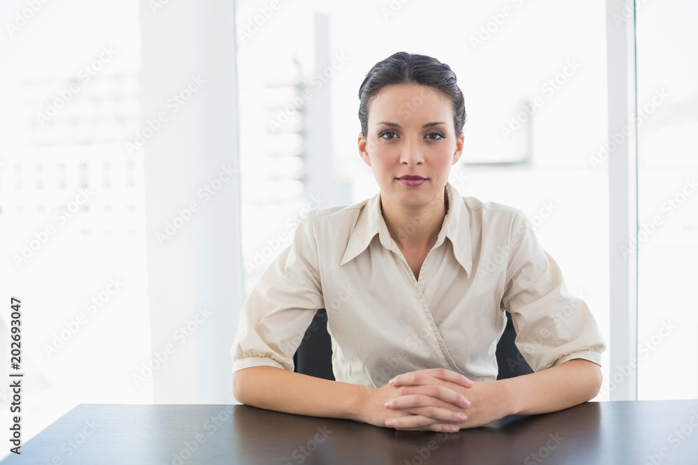 Serious stylish brunette businesswoman looking at camera and joining her hands Serious stylish brunette businesswoman looking at camera and joining her hands