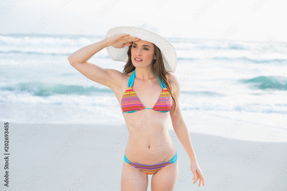 Pensive slim brown haired model in coloured bikini looking around her