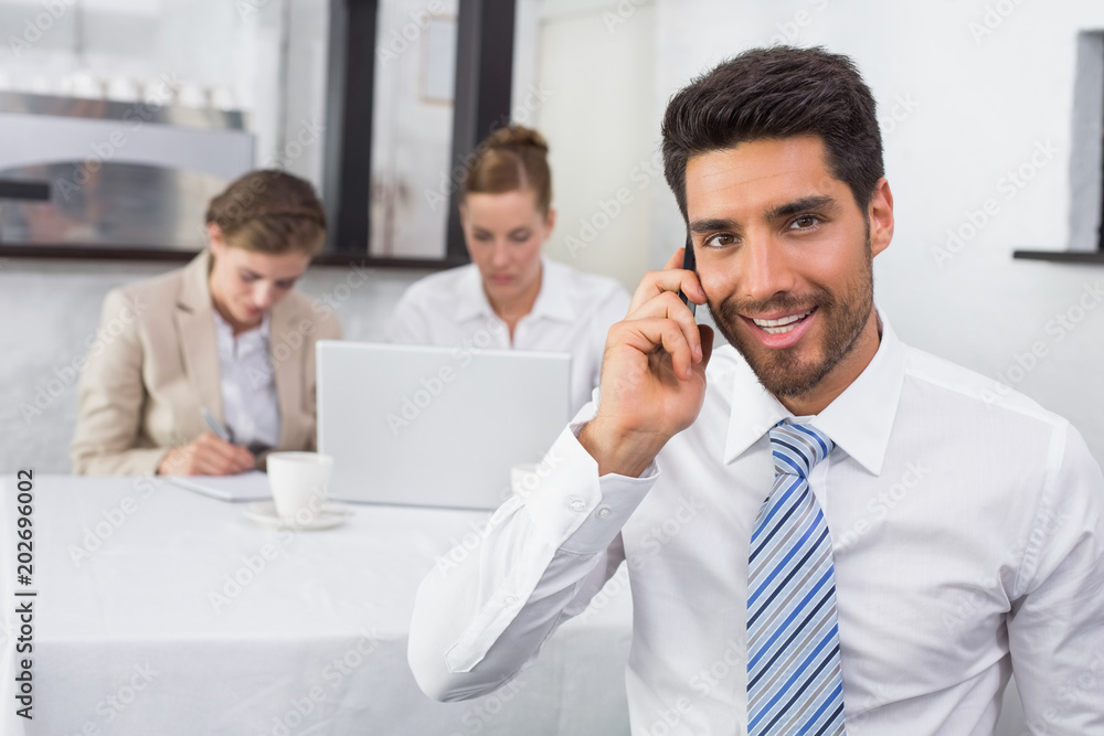 Businessman using mobile phone with colleagues at office desk Businessman using mobile phone with colleagues at office desk