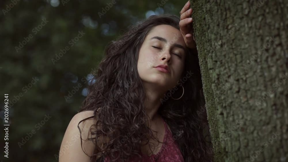 Pensive sad young brunette leaning against a tree Pensive sad young brunette leaning against a tree