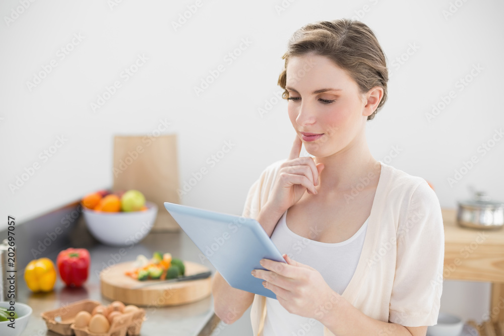 Concentrating young woman using her tablet standing in her kitchen Concentrating young woman using her tablet standing in her kitchen