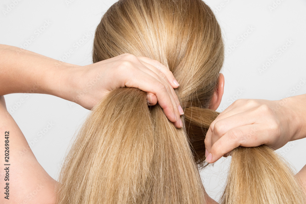 Fototapeta premium Gorgeous blonde woman braids her hair from behind