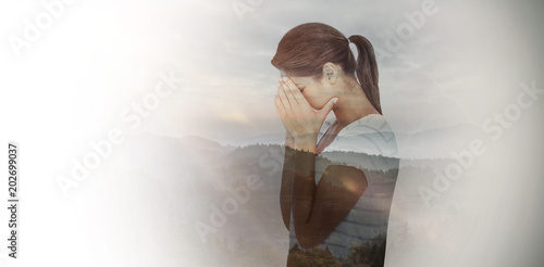Side view of upset woman covering face against trees and mountain range against cloudy sky