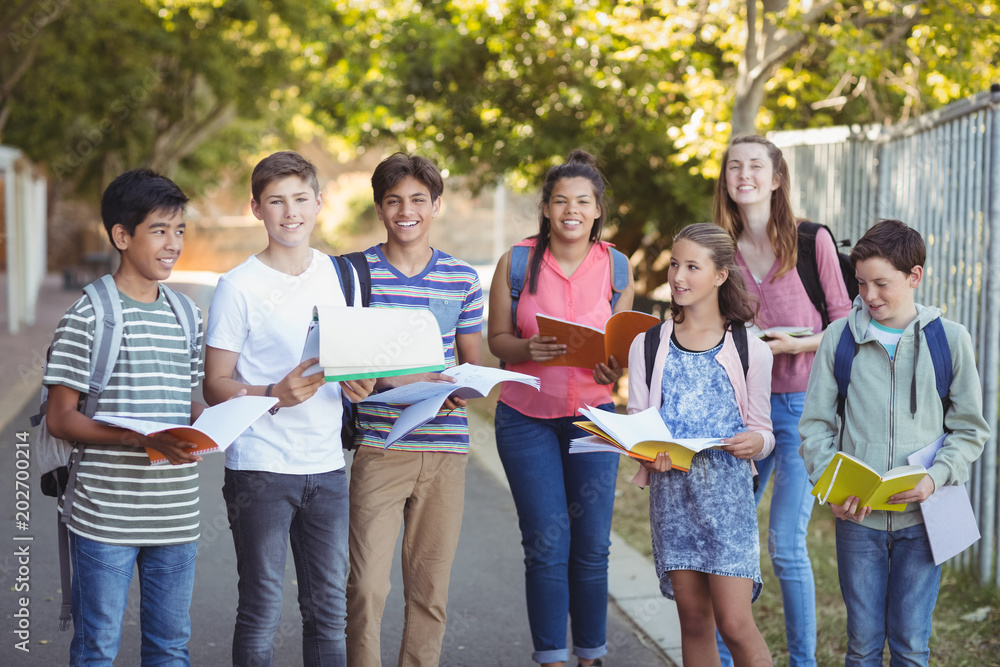 Portrait of happy students standing with books on road