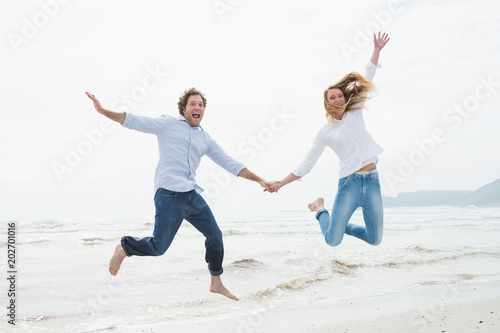 Cheerful couple holding hands and jumping at beach