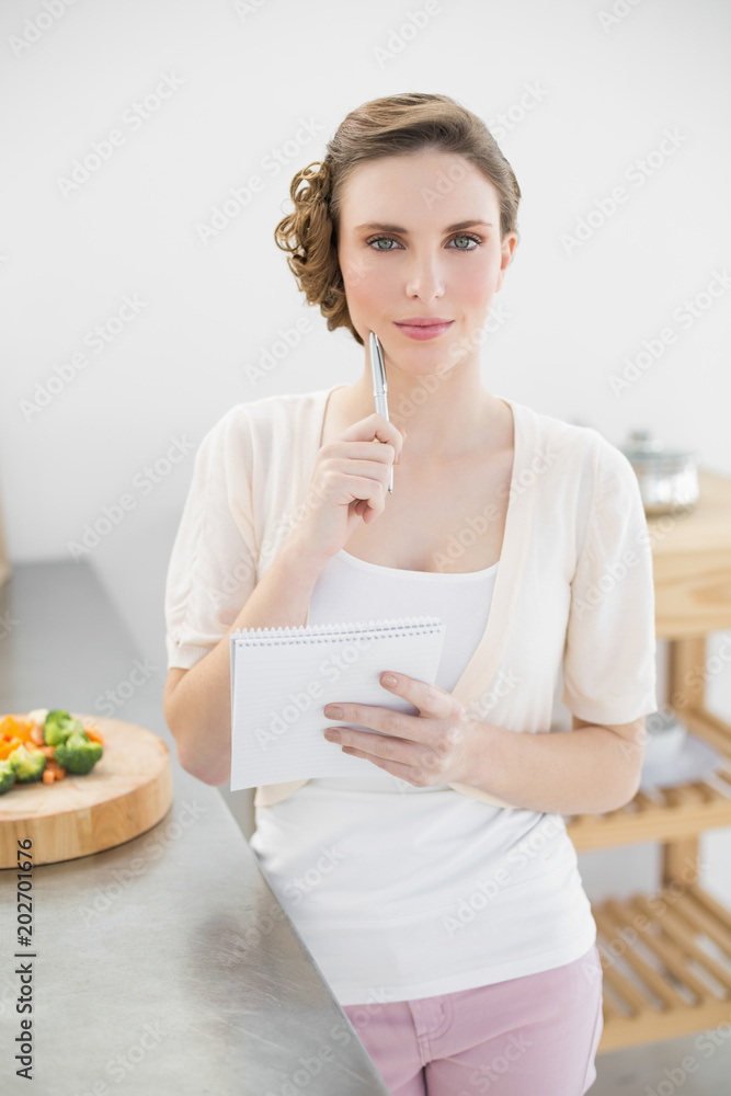 Beautiful thinking woman writing a shopping list standing in kitchen Beautiful thinking woman writing a shopping list standing in kitchen
